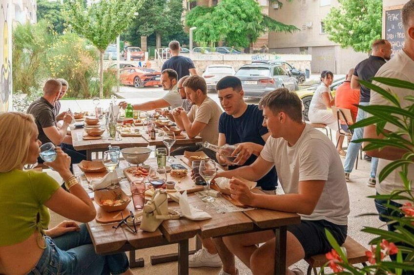 A group of people dining outdoors at a wooden table with various dishes and drinks. 5