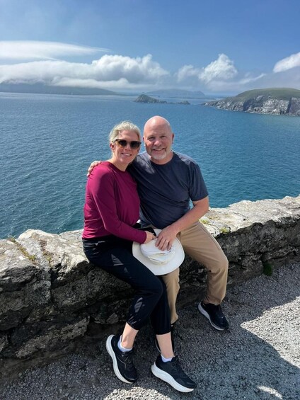 Two people sitting on a stone wall by a body of water with a mountainous landscape in the background. 5