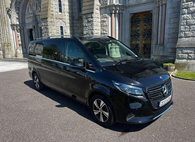 A black minivan parked in front of a stone building with ornate doors. 3