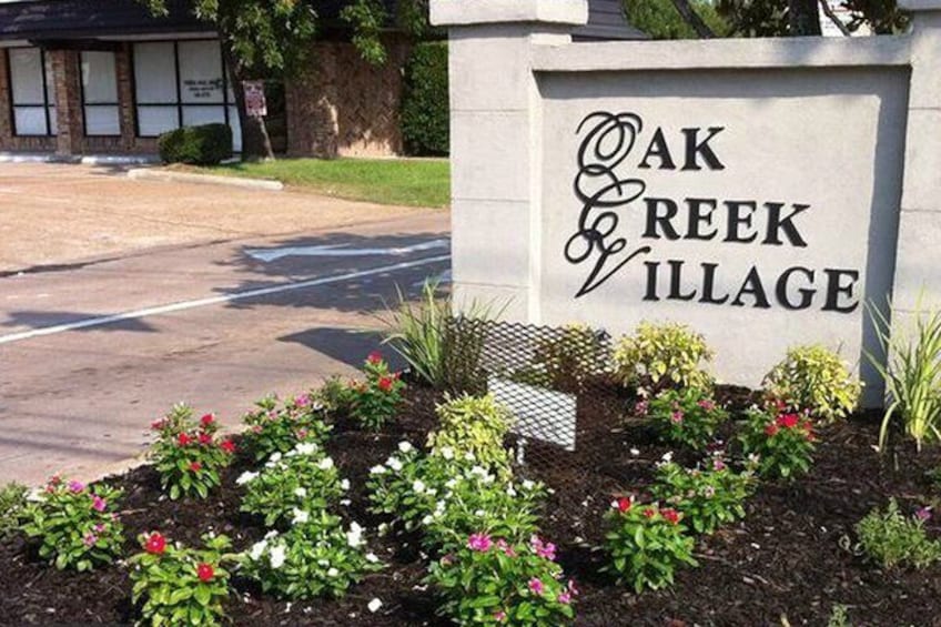 A sign for Oak Creek Village with a landscaped garden in front. 4