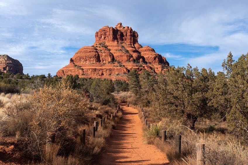 A dirt path leading to a large red rock formation. 1
