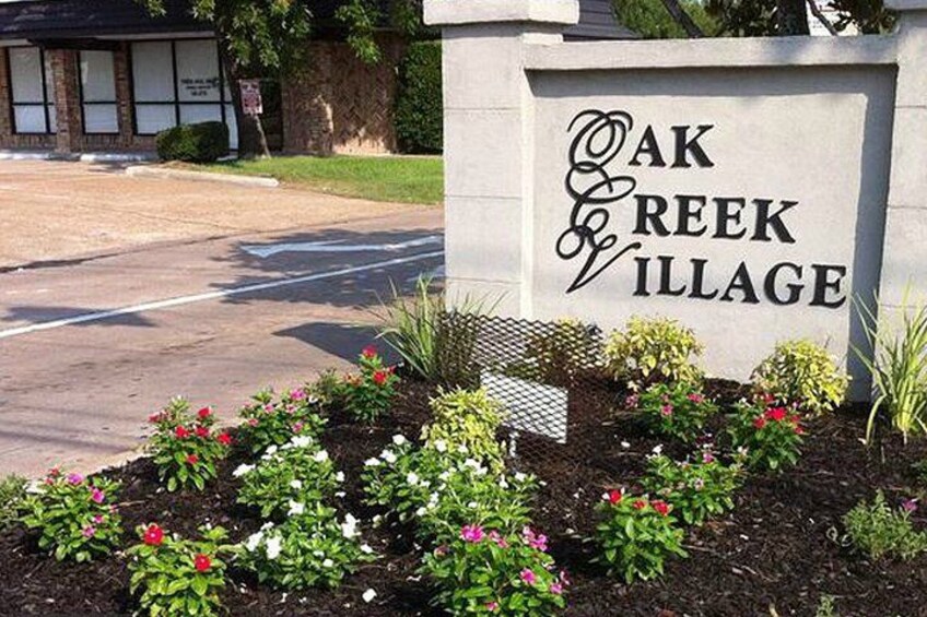 A sign for Oak Creek Village with a landscaped garden in front. 4