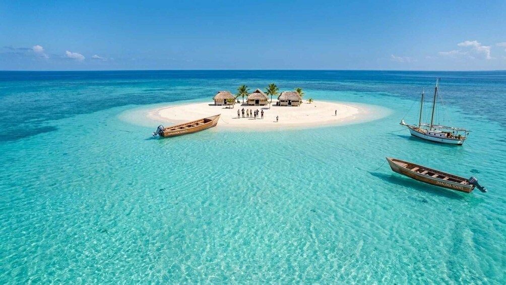 A tropical island with clear turquoise waters, surrounded by boats, and a small settlement with thatched-roof huts. 1