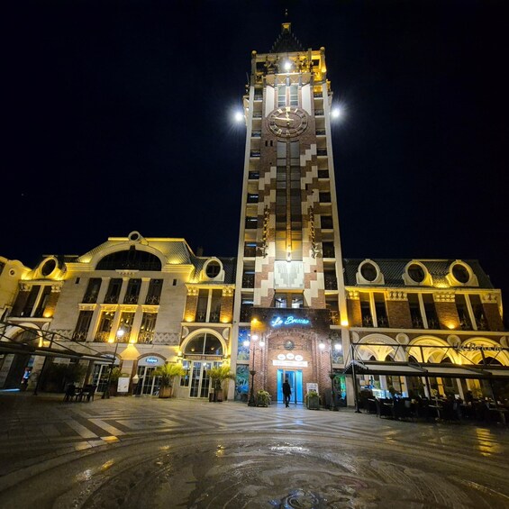 A large clock tower with illuminated numbers and hands, surrounded by a plaza with wet ground, reflecting lights. 4
