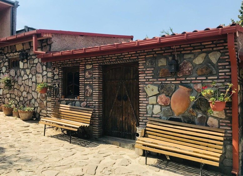 A stone building with a red roof, wooden benches, and potted plants. 2