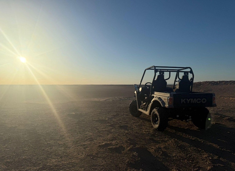 A Kymco vehicle parked on a desert road with the sun setting in the background. 1