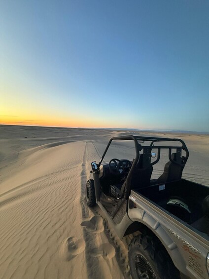 A 4x4 vehicle parked on a sand dune with a clear sky in the background. 4