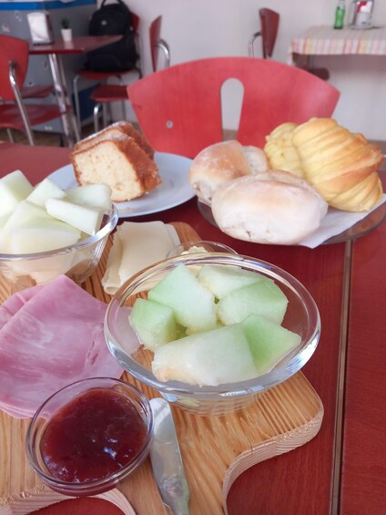 A table with various food items including bread, buns, and a bowl of melon. 3