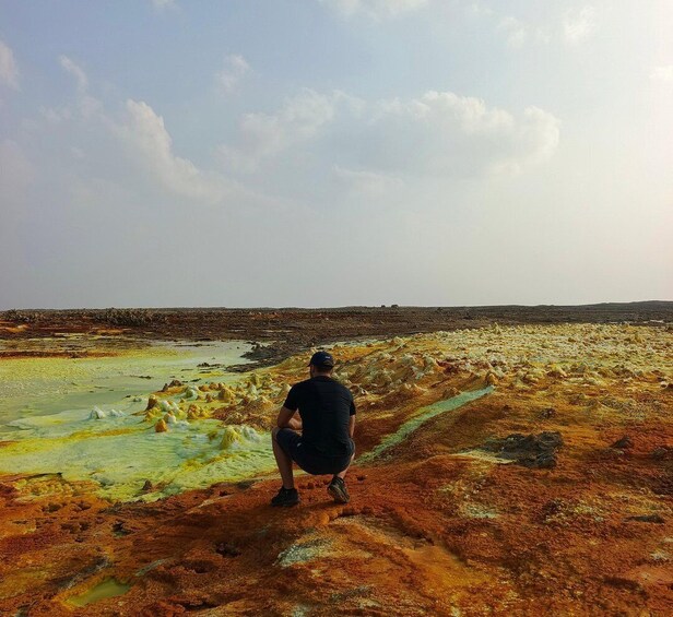 A person sitting on a colorful mineral-rich terrain with a vast landscape in the background. 2