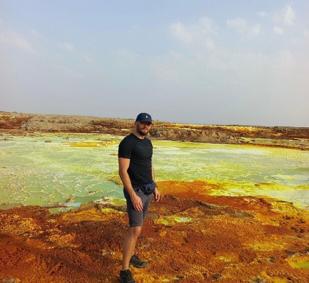 A person standing in a geothermal area with colorful mineral deposits. 3