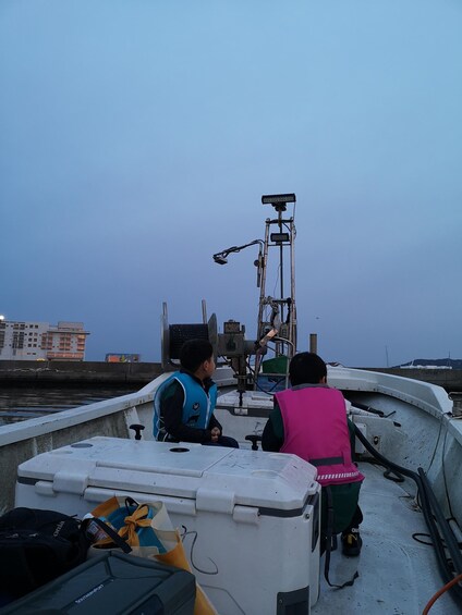 Two people on a boat with a winch and a container. 3