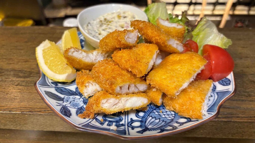 A plate of breaded and fried fish, lemon wedges, a salad, and a side of tartar sauce. 4