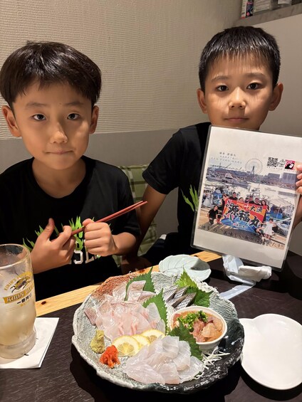 Two individuals at a restaurant with a plate of sashimi, a drink, and a menu. 2