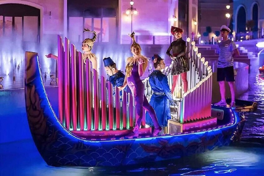 A group of people on a stage with a boat-like structure, illuminated by colorful lights. 3