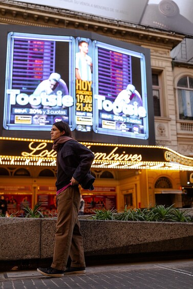 A person standing in front of a theater marquee advertising a show. 3