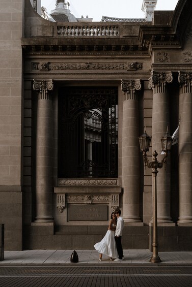 A couple standing in front of a building with columns and a sign that reads 'Patacio San Marti.' 1