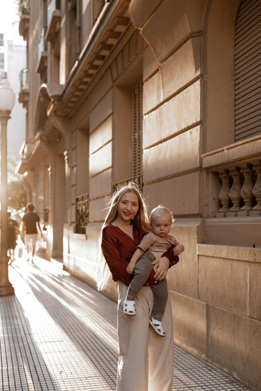 A woman holding a child on a city street with buildings and a lamppost. 2