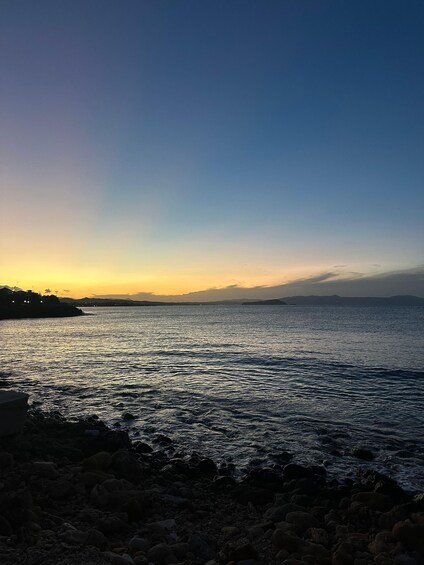A sunset over a calm sea with rocky shores and distant mountains. 3