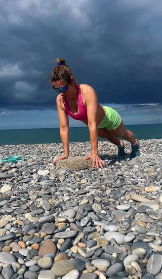 A person doing a push-up on a pebbled beach with a cloudy sky in the background. 2