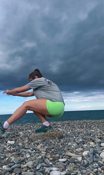 A person crouching on a pebbled beach with the ocean and a cloudy sky in the background. 4