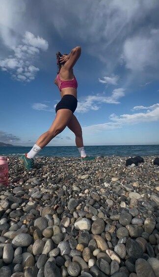 A person jumping on a pebble beach with the sea and sky in the background. 1