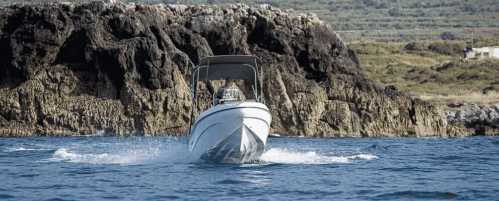 A white boat moving through water with a rocky coastline in the background. 2