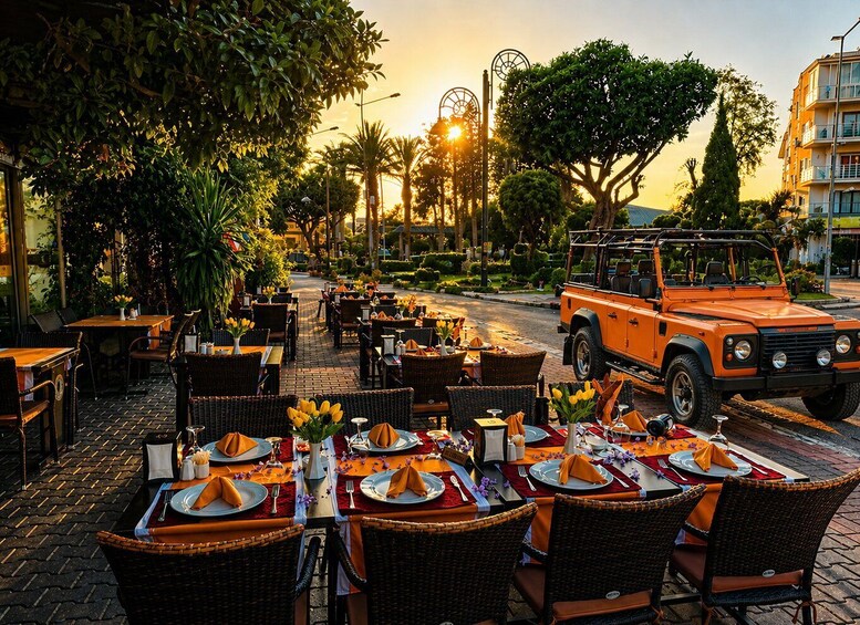 An outdoor restaurant with tables set for dining, surrounded by lush greenery and a parked vehicle. 4