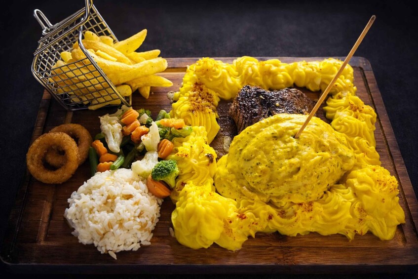 A meal with rice, vegetables, a steak, and French fries on a wooden board. 5