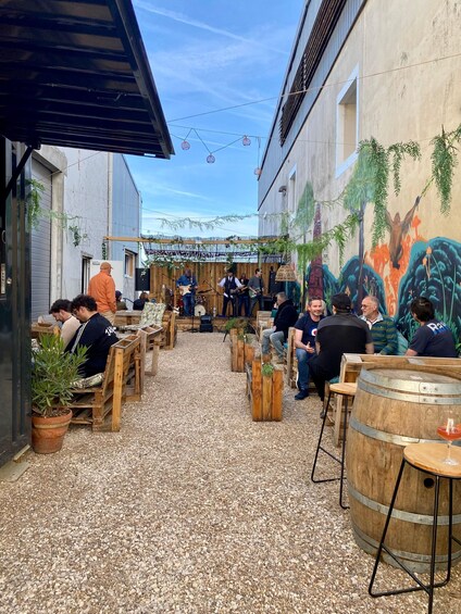 An outdoor venue with wooden tables and chairs, a band performing, and a mural on the wall. 2