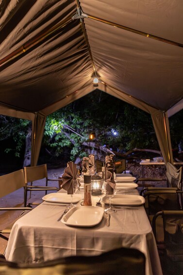 A tented dining area with tables set for a meal, surrounded by trees. 4