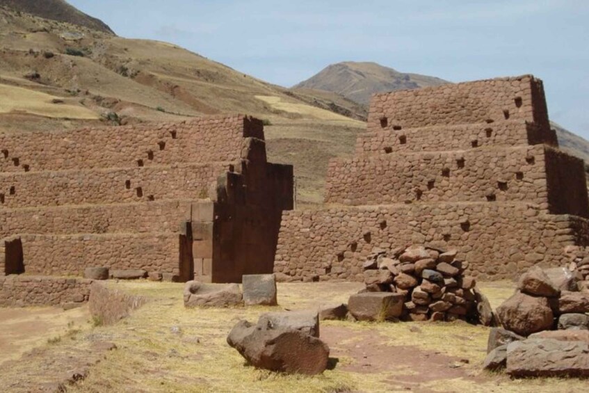 Ancient stone ruins with stepped structures and a pile of rocks in a dry, hilly landscape. 3