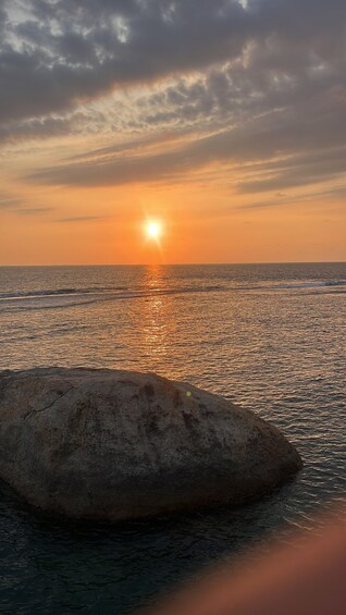 A sunset over a calm sea with a large rock in the foreground. 2