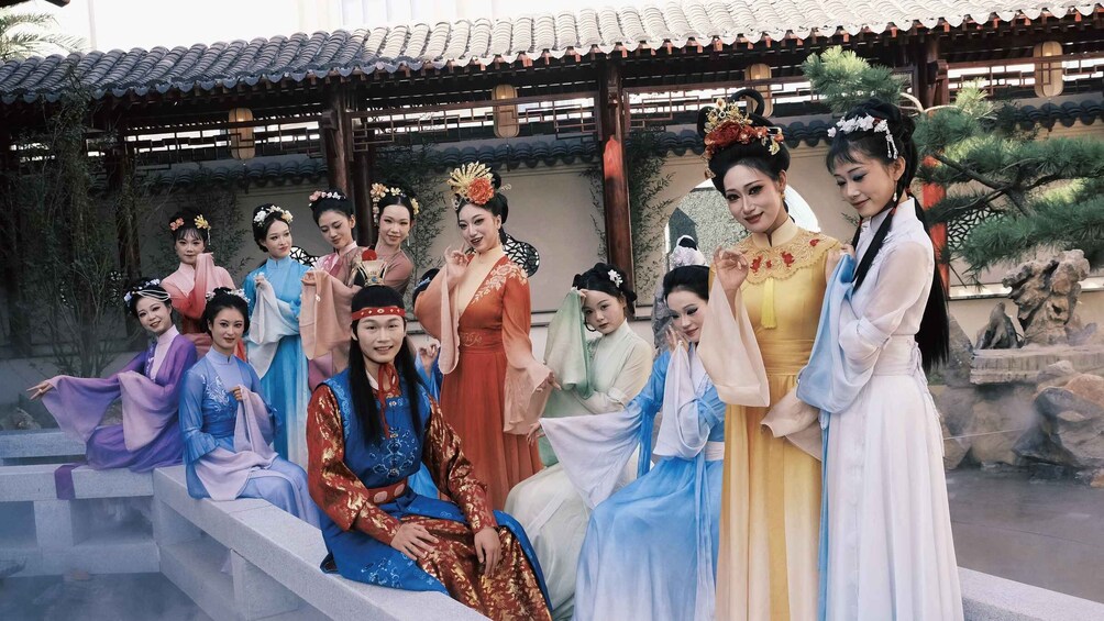 A group of people in traditional attire, seated and standing in an outdoor setting with a tiled roof structure and stone steps. 5