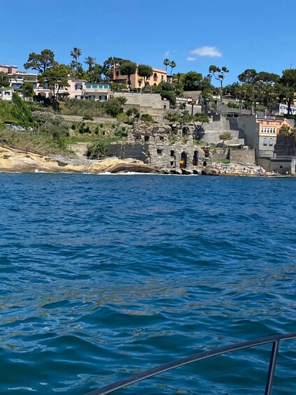 A coastal town with buildings on a hillside, rocky shoreline, and calm sea. 5