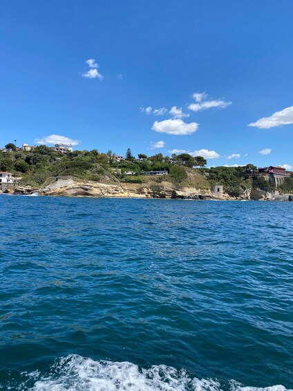 A coastal landscape with clear blue waters, rocky shorelines, and buildings on hills. 3