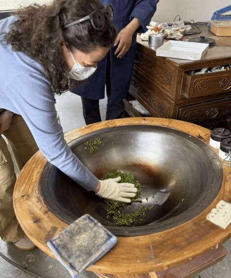 A person handling green leaves in a large metal bowl. 4
