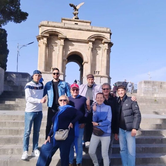 A group of people standing in front of a large stone archway with an eagle statue on top. 2
