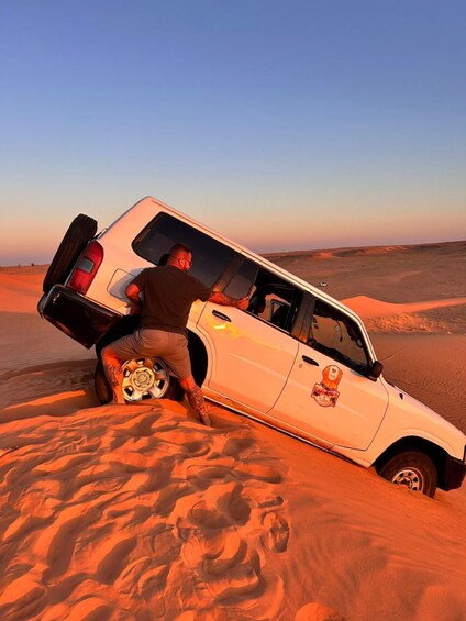 A white SUV stuck in a sand dune with a person attempting to free it. 4