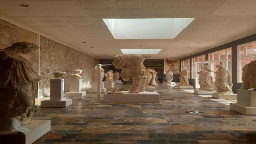 A museum corridor with classical sculptures on pedestals, patterned walls, and a skylight. 5