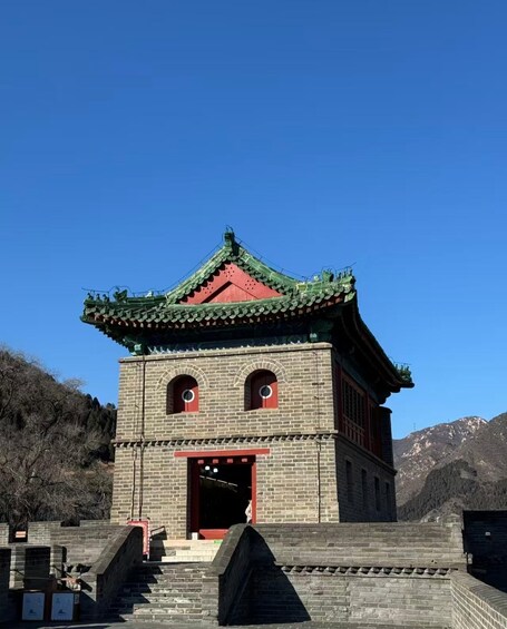 Un bâtiment traditionnel chinois, doté d’un toit végétalisé et de touches de couleur rouge, se dressant sur un fond de paysage montagneux. 3