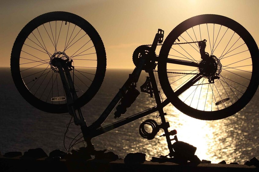 A bicycle leaning against rocks with a sunset in the background. 2