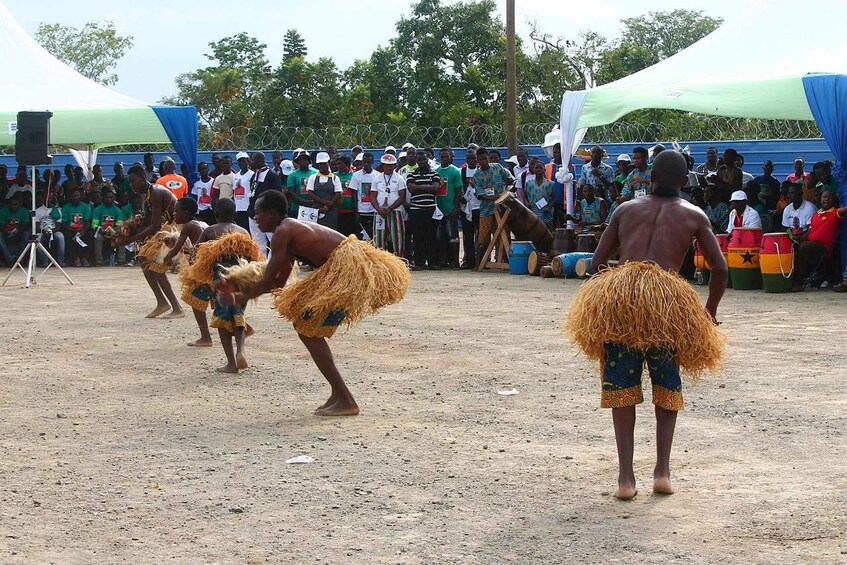 A group of people in traditional attire performing a dance in an outdoor setting with a crowd watching. 2