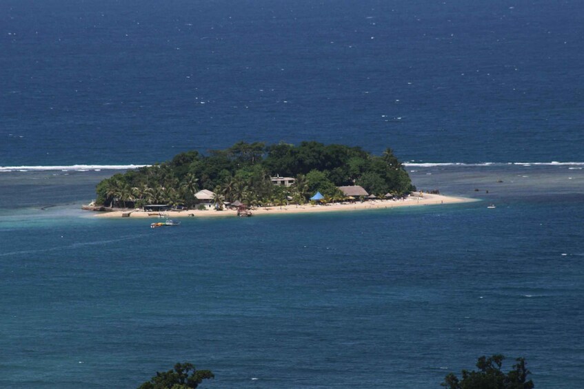 A tropical island with a beach, clear blue waters, and a few boats. 3