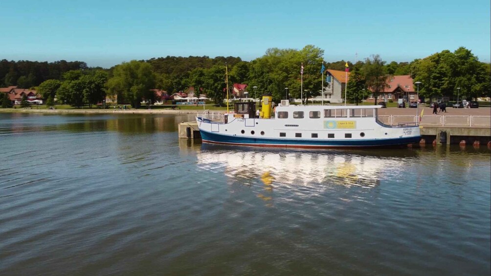 A white and blue boat docked at a pier with a forested hillside in the background. 5