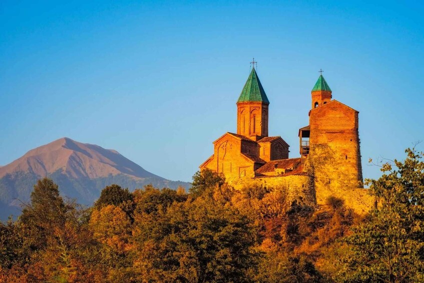 A historic church with two towers, set against a backdrop of a mountain and autumn foliage. 1