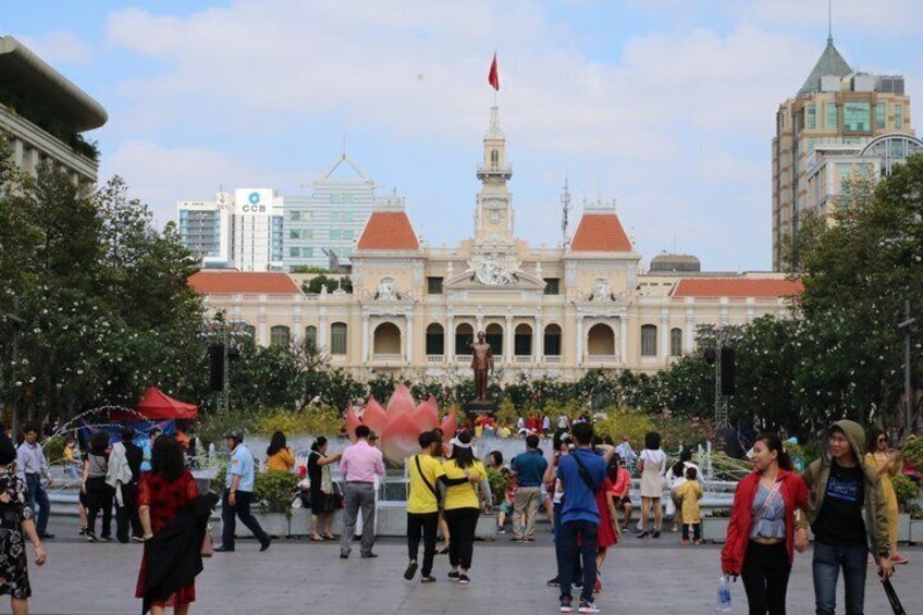 A busy public square with a historic building featuring a clock tower and a flag. 3