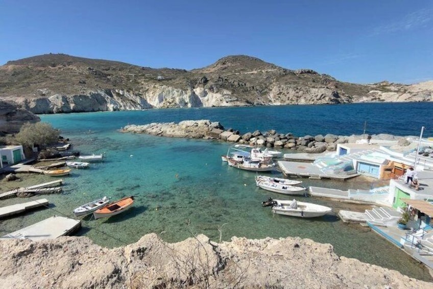 A coastal harbor with boats docked, rocky terrain, and clear blue water. 1