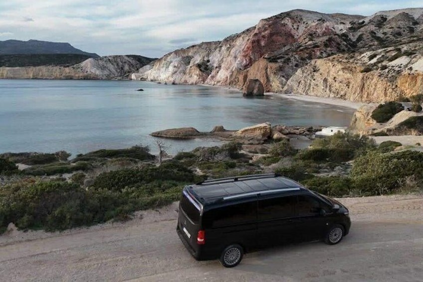 A black van parked on a dirt road beside a coastal area with rocky cliffs and a calm sea. 5