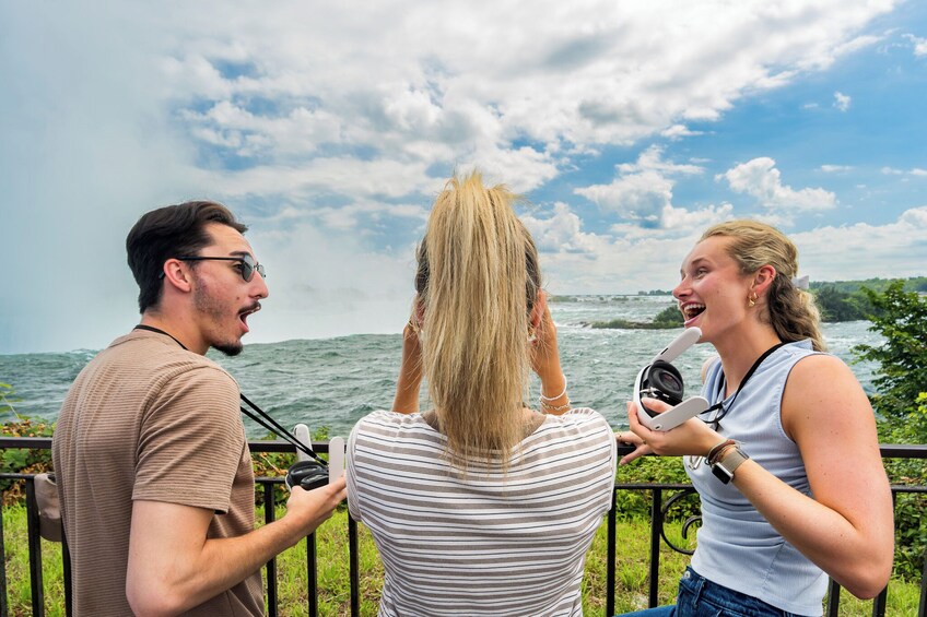 Three people standing by a railing, facing a body of water with a bridge in the distance. 1