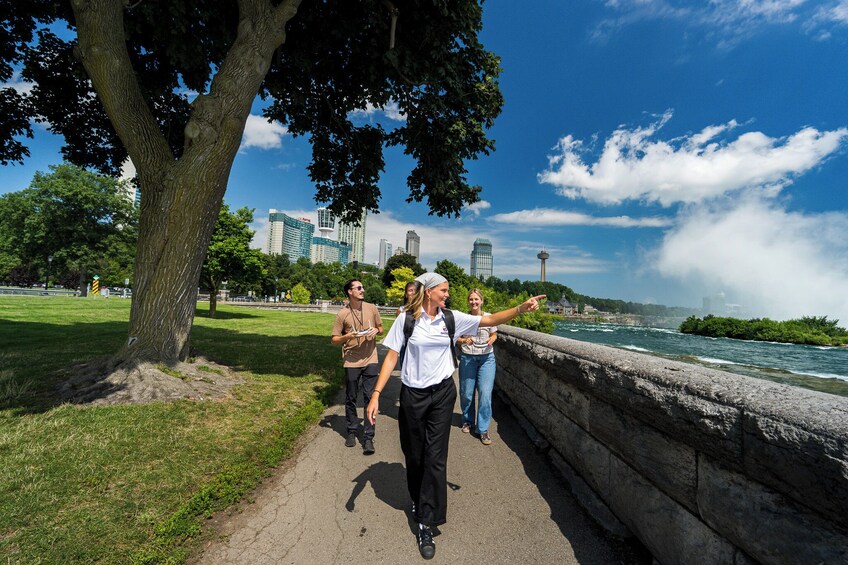 A group of people walking along a riverside path with a city skyline in the background. 3